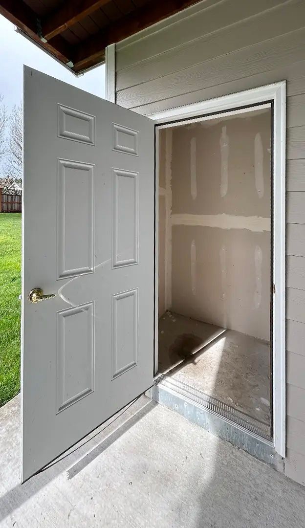 Open white exterior door leading into an unfinished interior closet or small room.