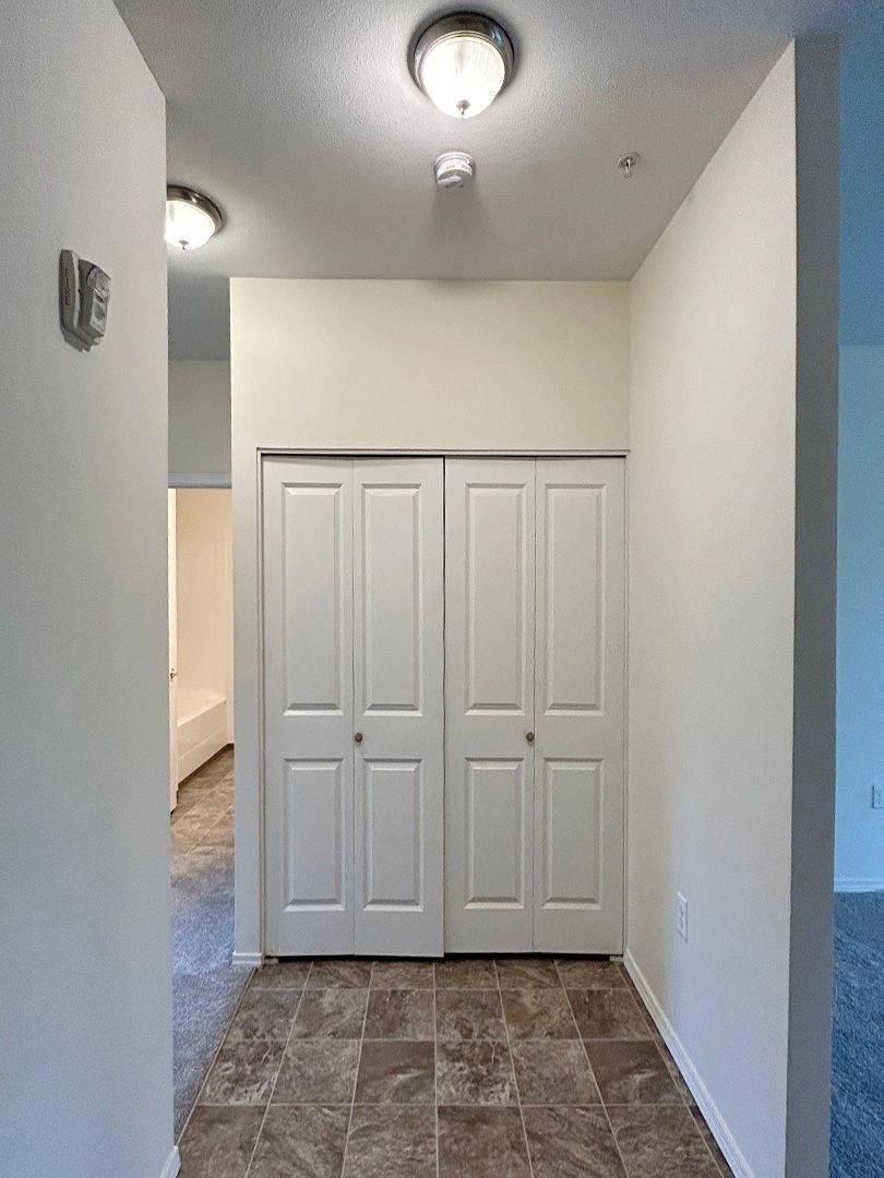Hallway with tiled floor, white walls, ceiling light, and double closet doors at the end.