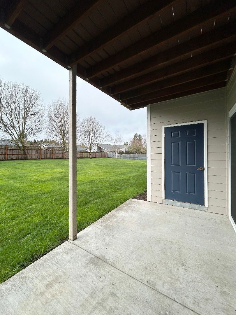 Covered concrete patio beside a blue door, overlooking a grassy yard and leafless trees.