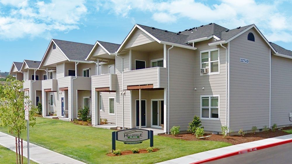 Apartment complex exterior with beige siding, balconies, and a manicured lawn under a blue sky