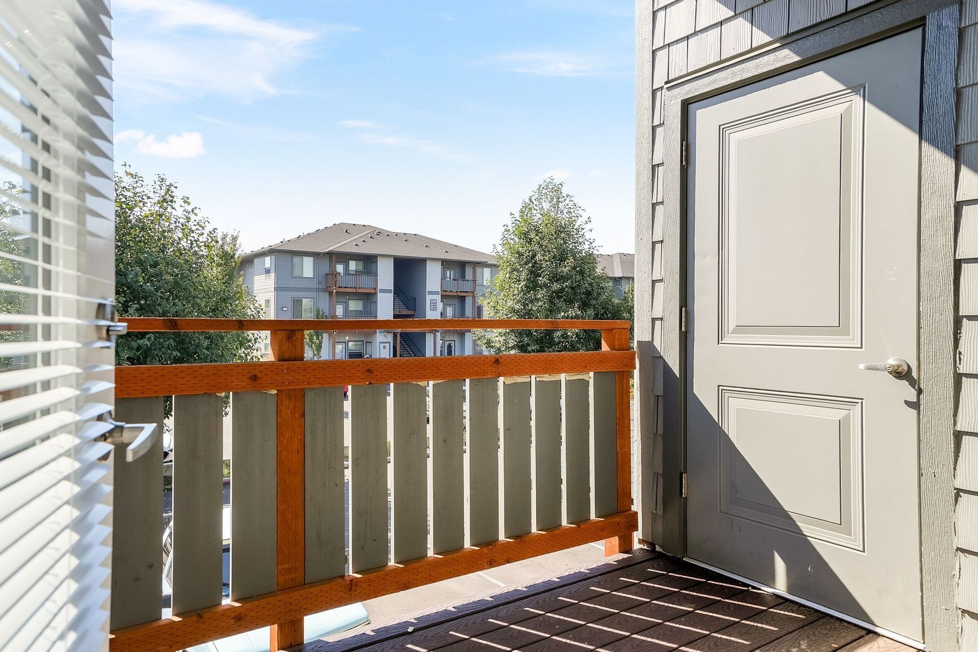 Balcony with white railing and open door, overlooking apartment buildings in bright sunlight