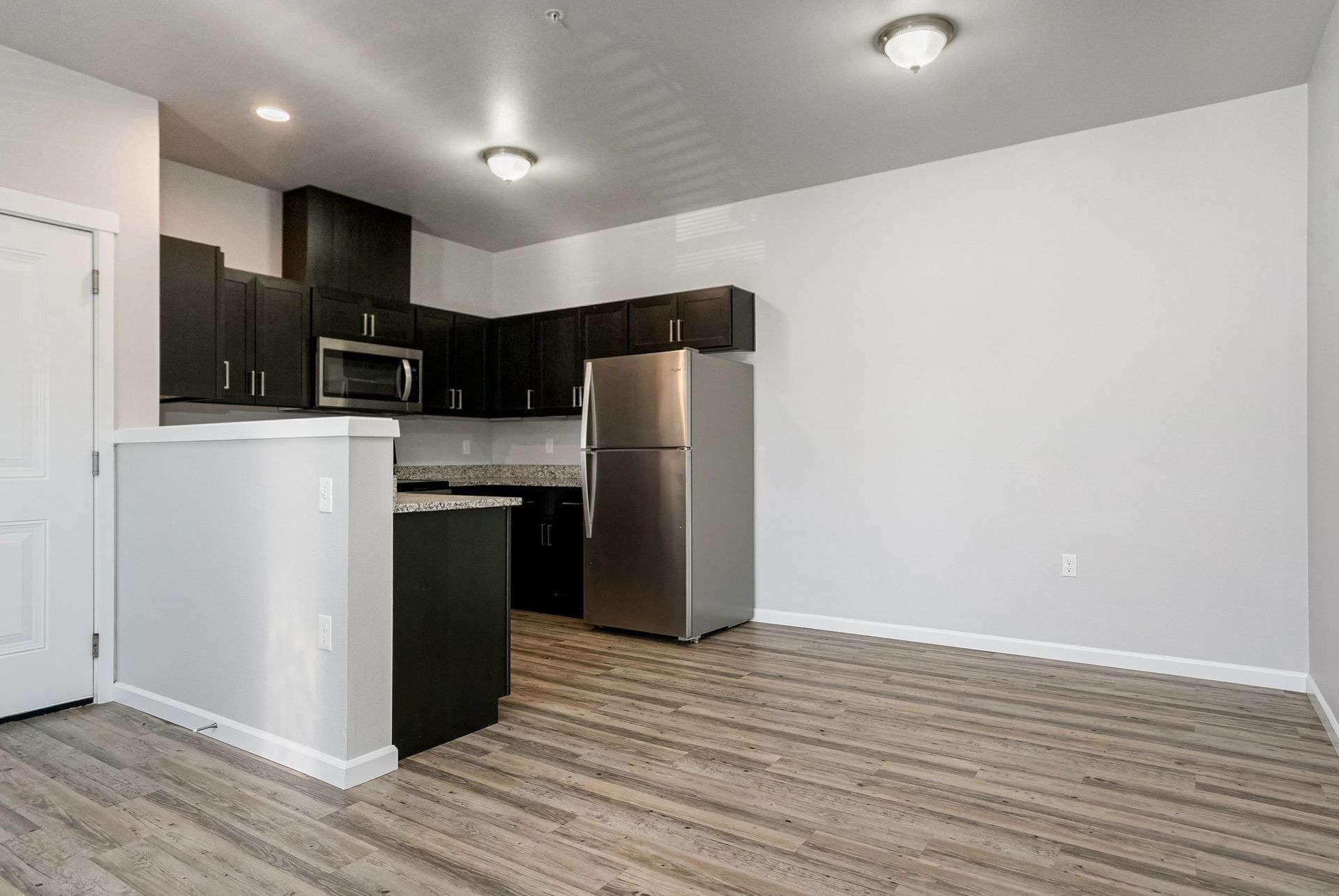 Empty modern kitchen with dark cabinets, stainless appliances, and wood-look flooring