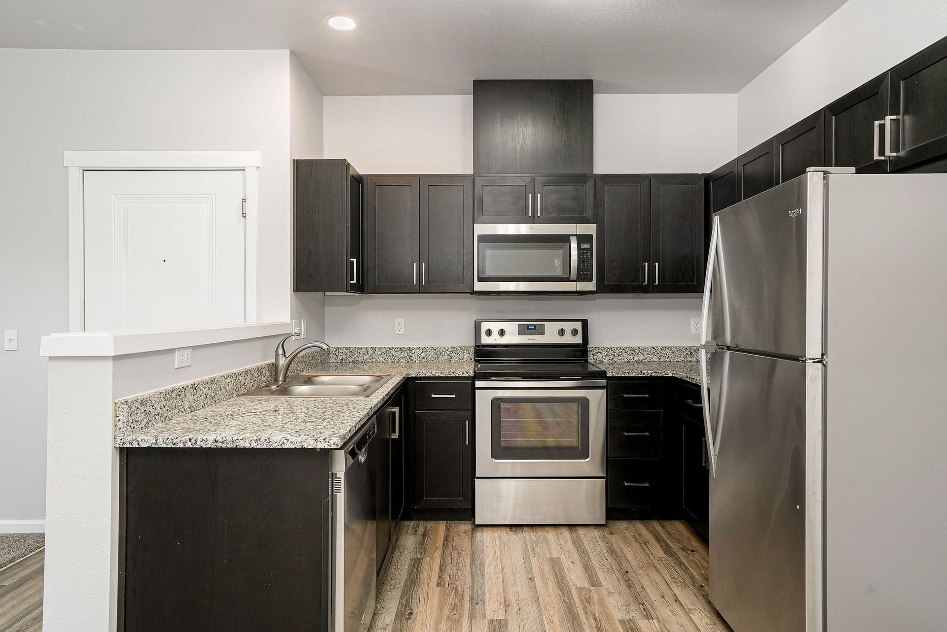 Modern kitchen with dark cabinets, granite counters, stainless steel appliances, and wood-look flooring