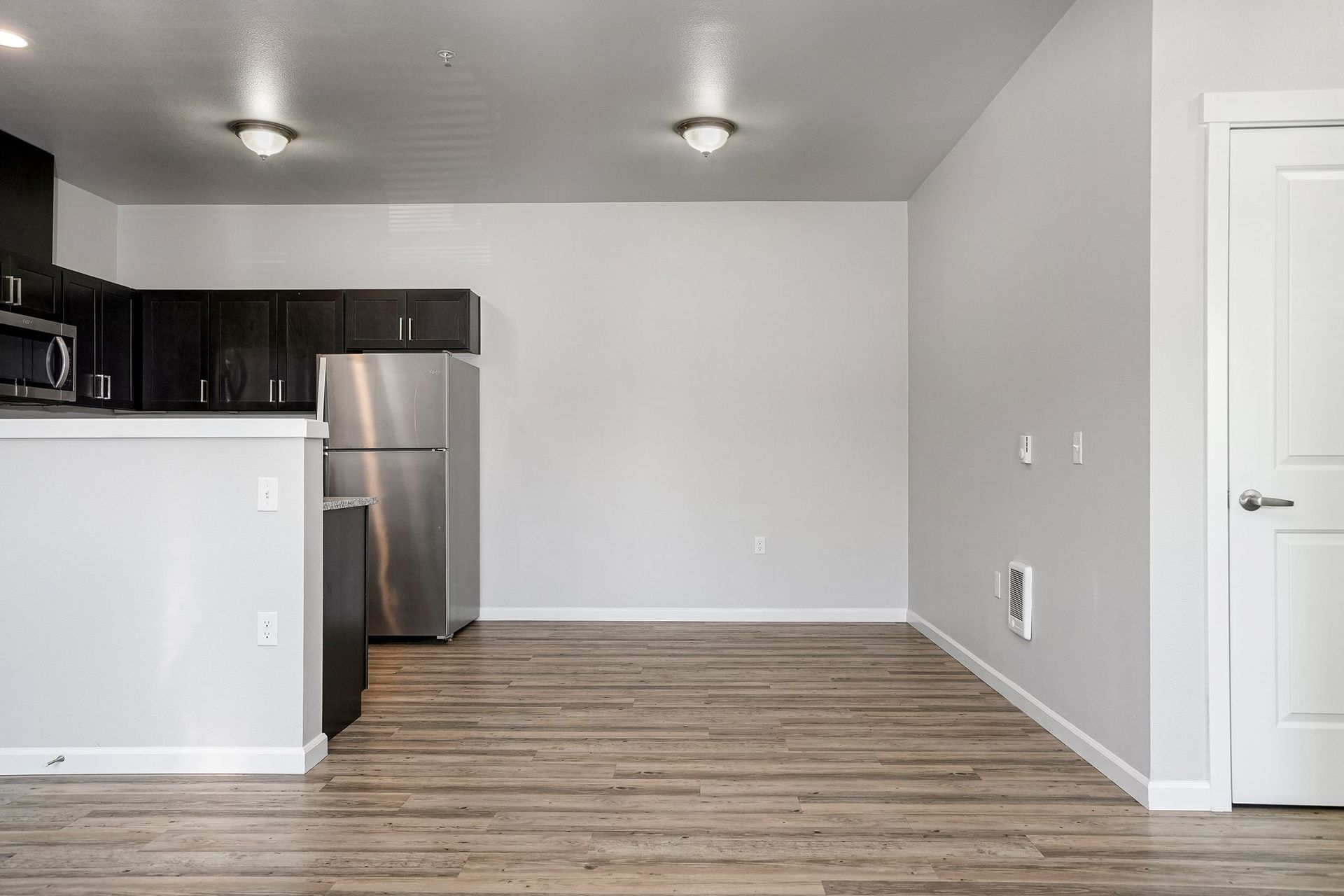 Empty modern apartment kitchen and living area with light wood floors, gray walls, and stainless steel appliances