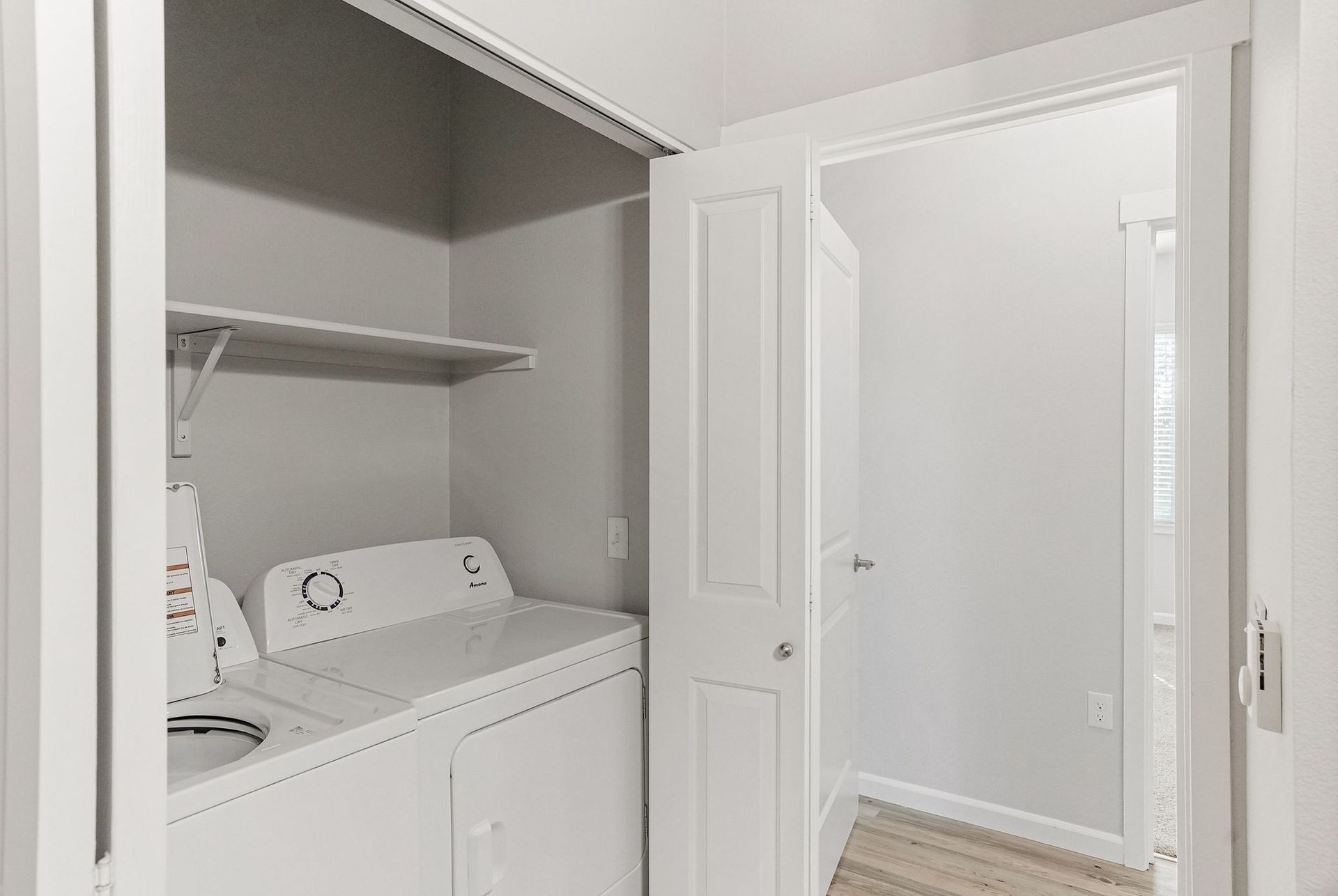 White laundry closet with stacked washer and dryer and open closet doors in a hallway