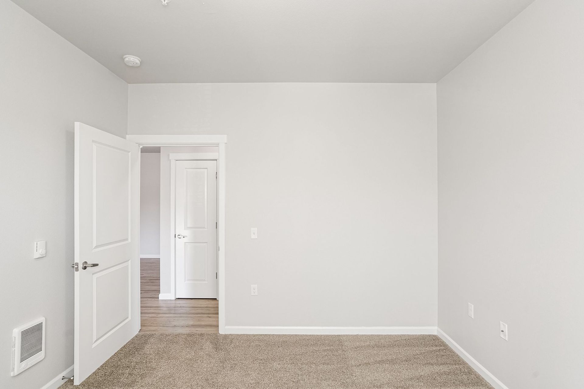 Empty white room with carpet, open doorways, and plain walls