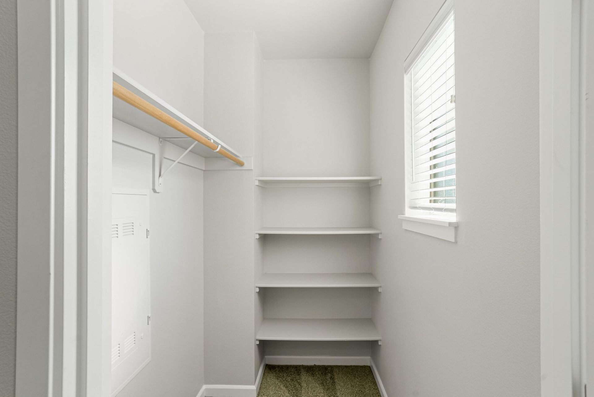 Empty white closet with shelves, hanging rod, and a window with blinds on the right.
