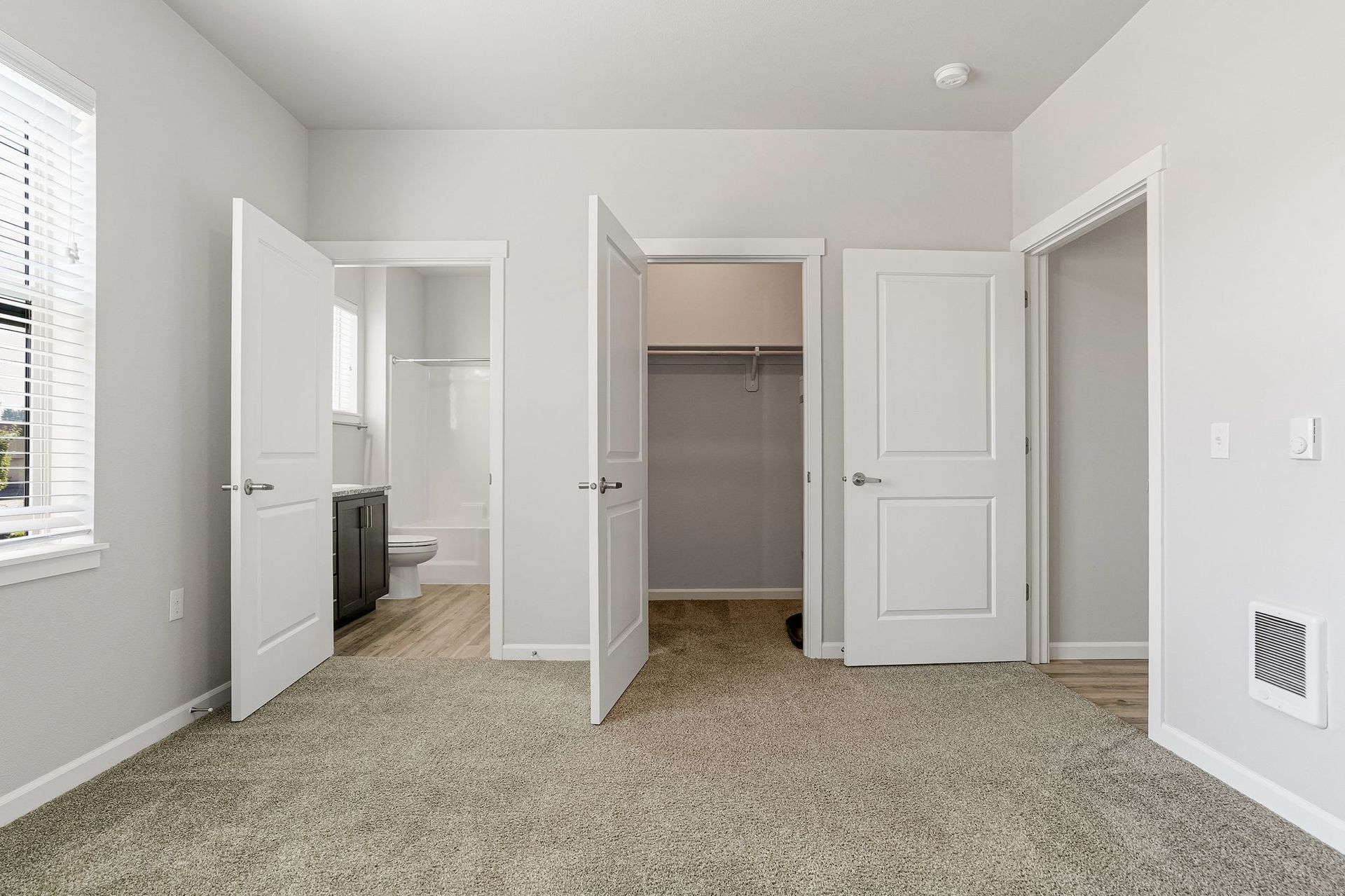 Empty beige bedroom with carpet, open closet, and bathroom door visible.