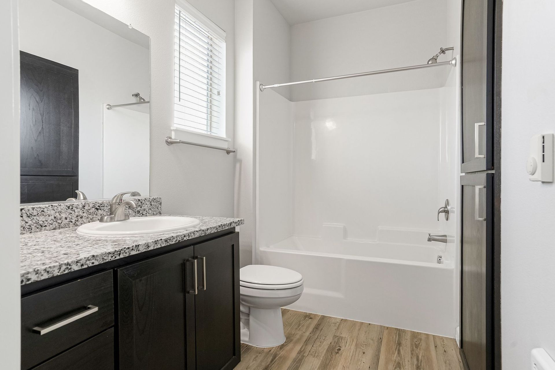 Modern bathroom with dark vanity, white tub-shower, toilet, and wood-look floor.