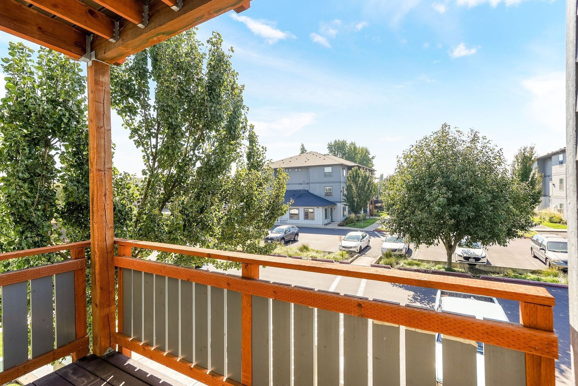 Wooden balcony overlooking a sunny residential street with trees and parked cars