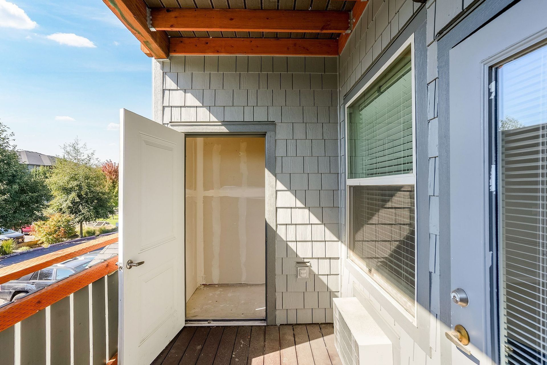 Small balcony with open white door, gray brick wall, and glass sliding door in sunlight