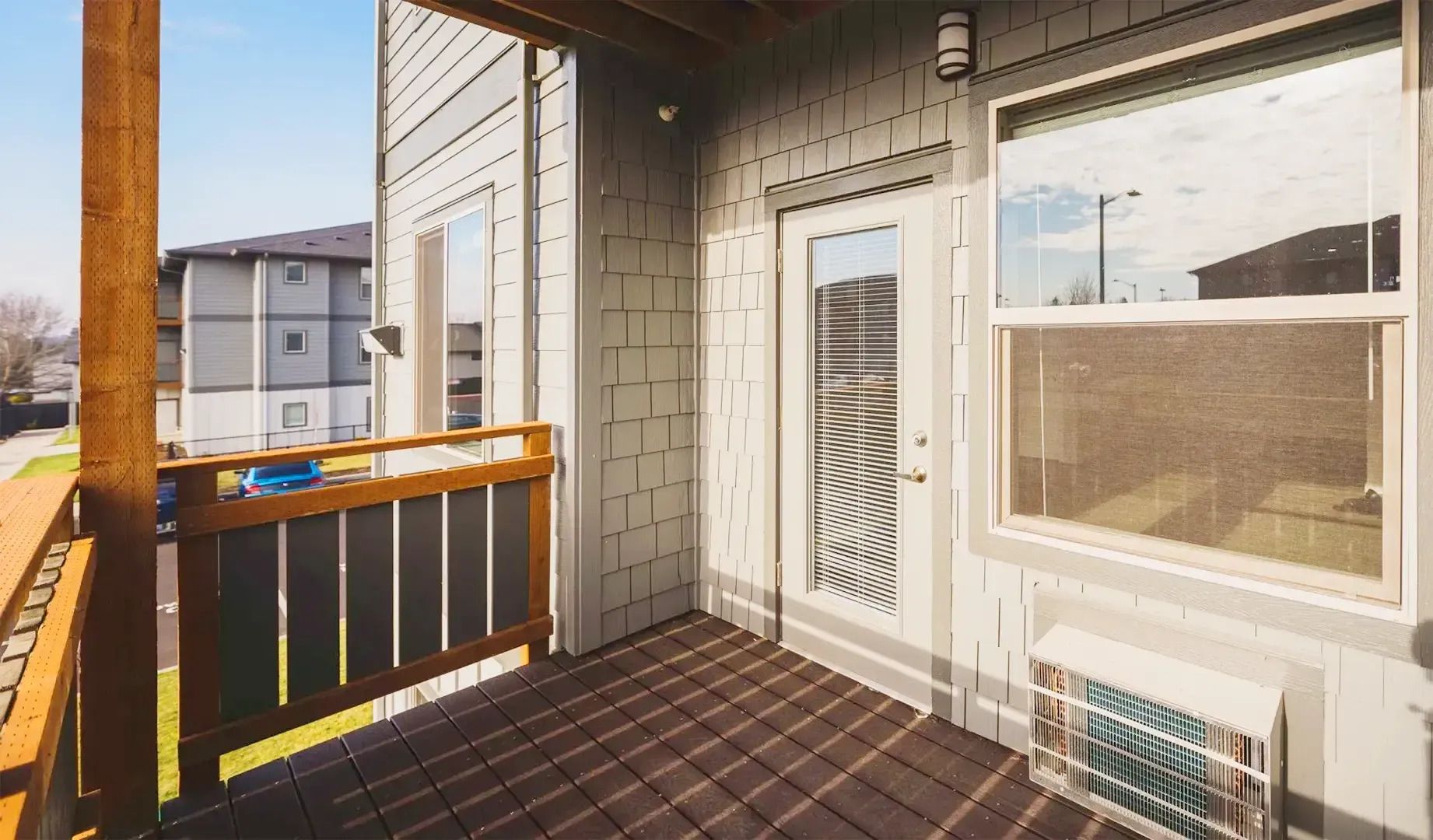 Sunny apartment balcony with black railing, white door, and large window overlooking neighboring buildings