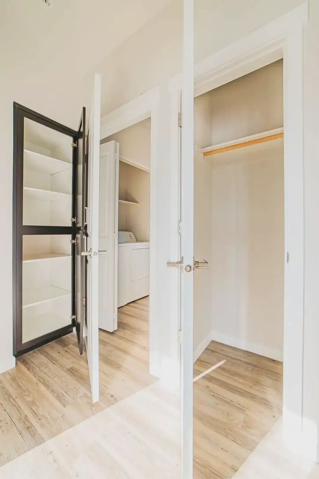 Bright white hallway with two open closet doors, one showing shelves and a sink, the other empty with a hanging rod.