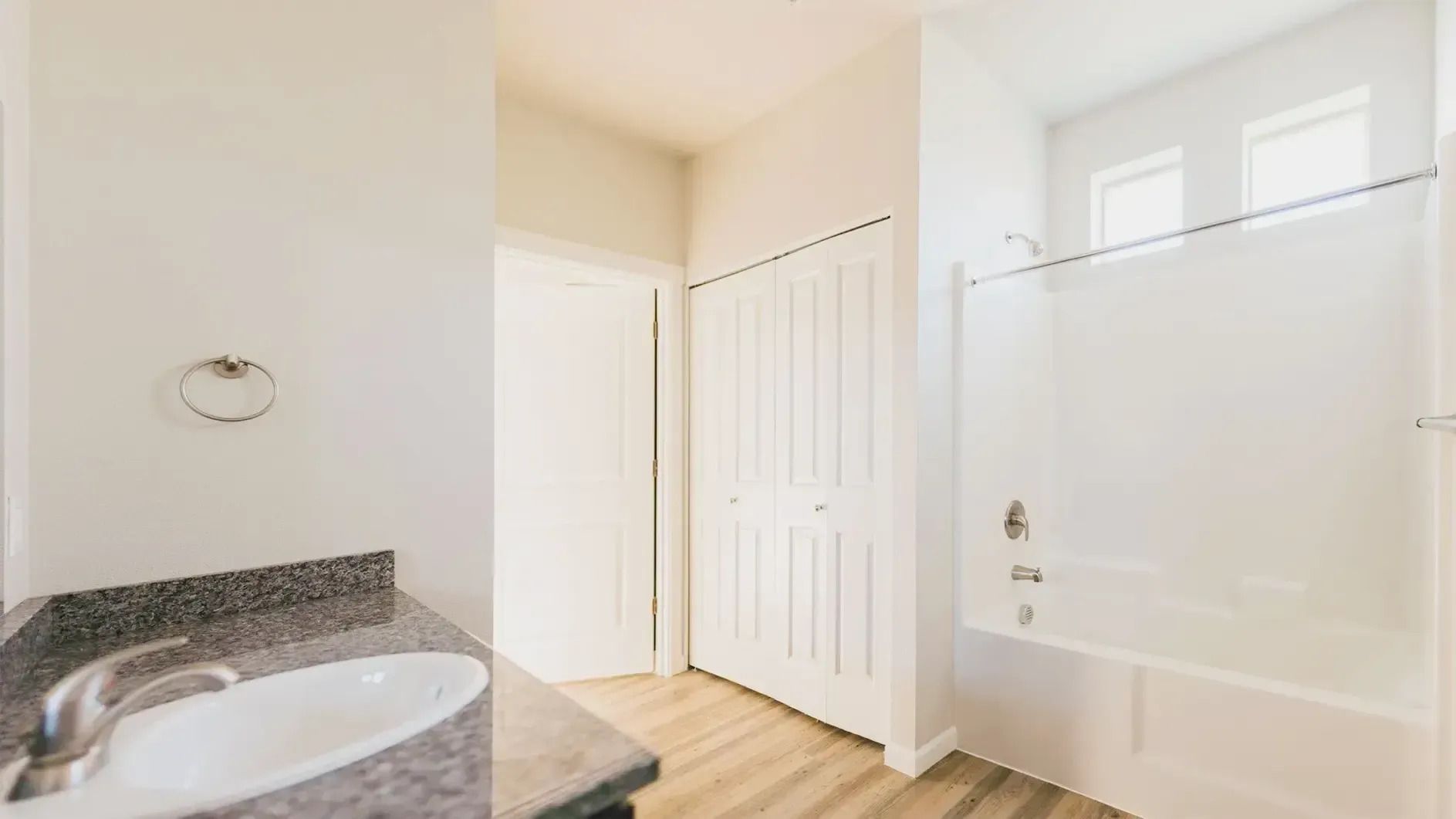 Bright bathroom with granite vanity, white cabinets, glass shower, and light wood floor.