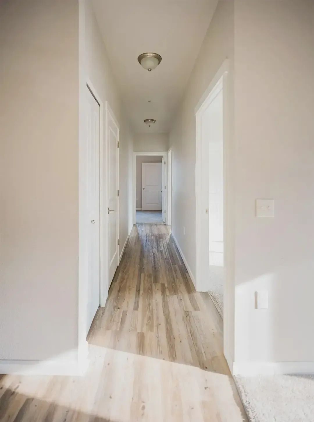 Bright empty hallway with white walls, wood floors, and doors on both sides.