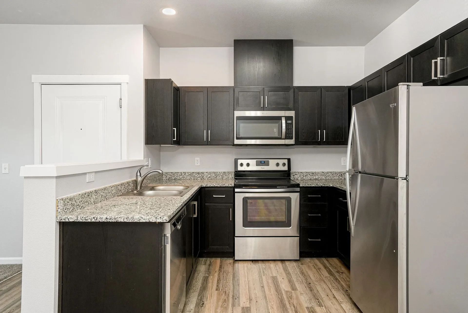 Modern kitchen with dark cabinets, stainless steel appliances, granite counters, and wood-look flooring