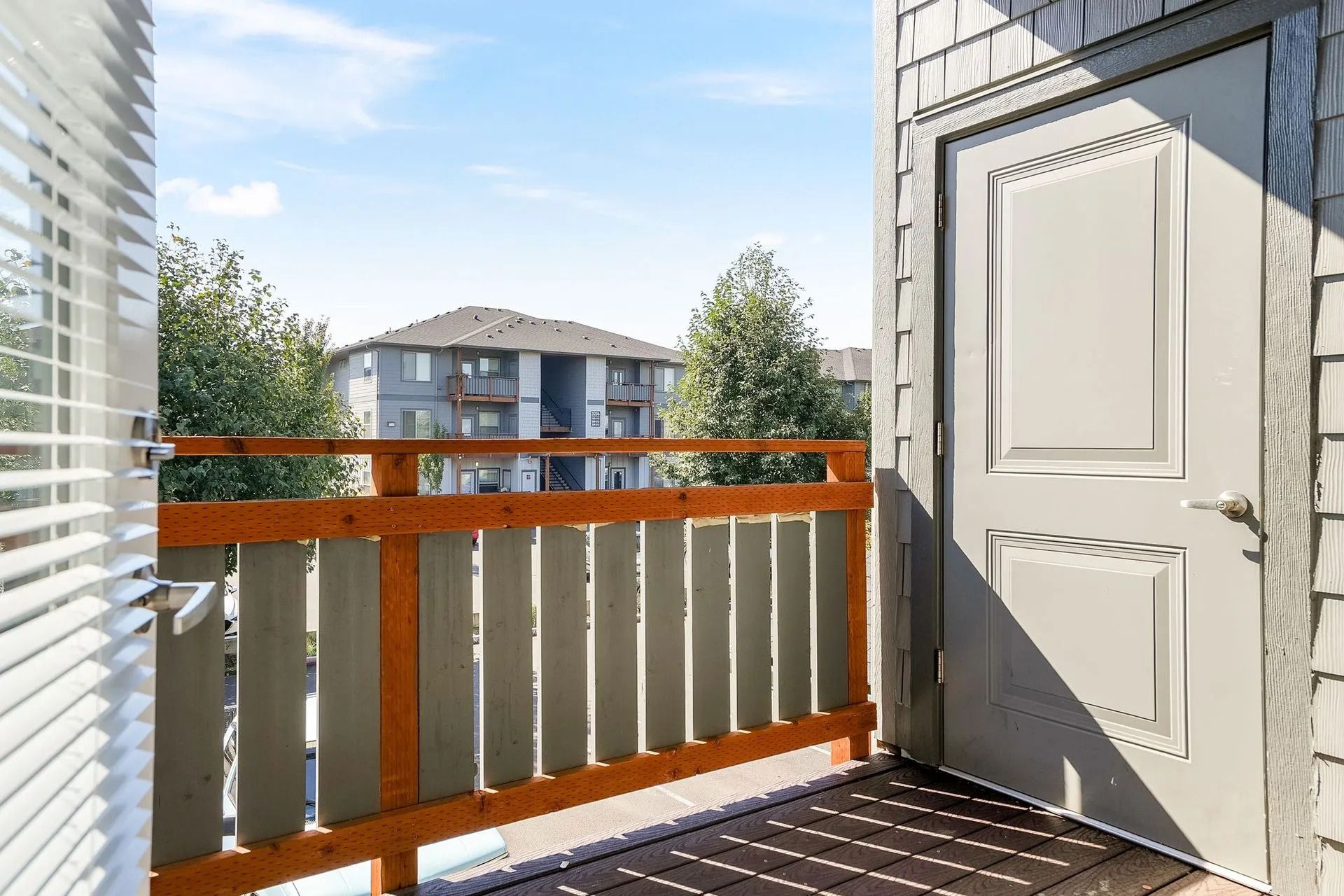 Apartment balcony with wooden railing, white door, and neighboring buildings in bright daylight