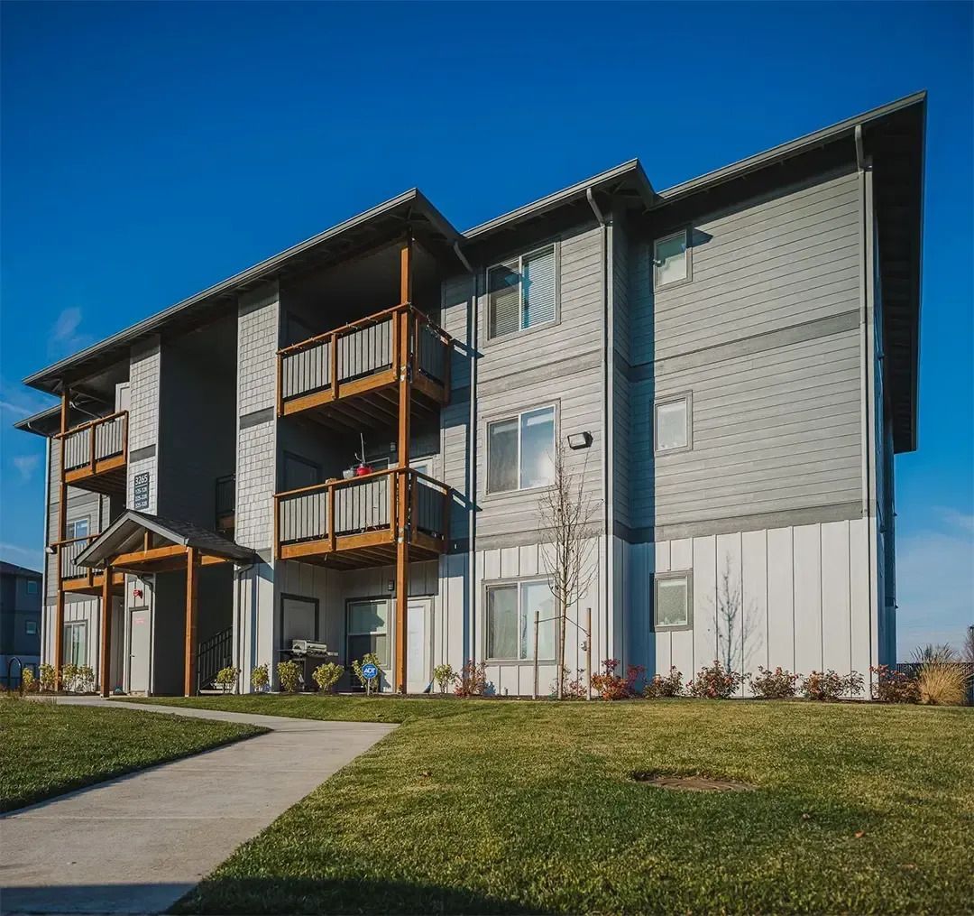 Modern apartment building with balconies and a grassy front lawn under a clear blue sky
