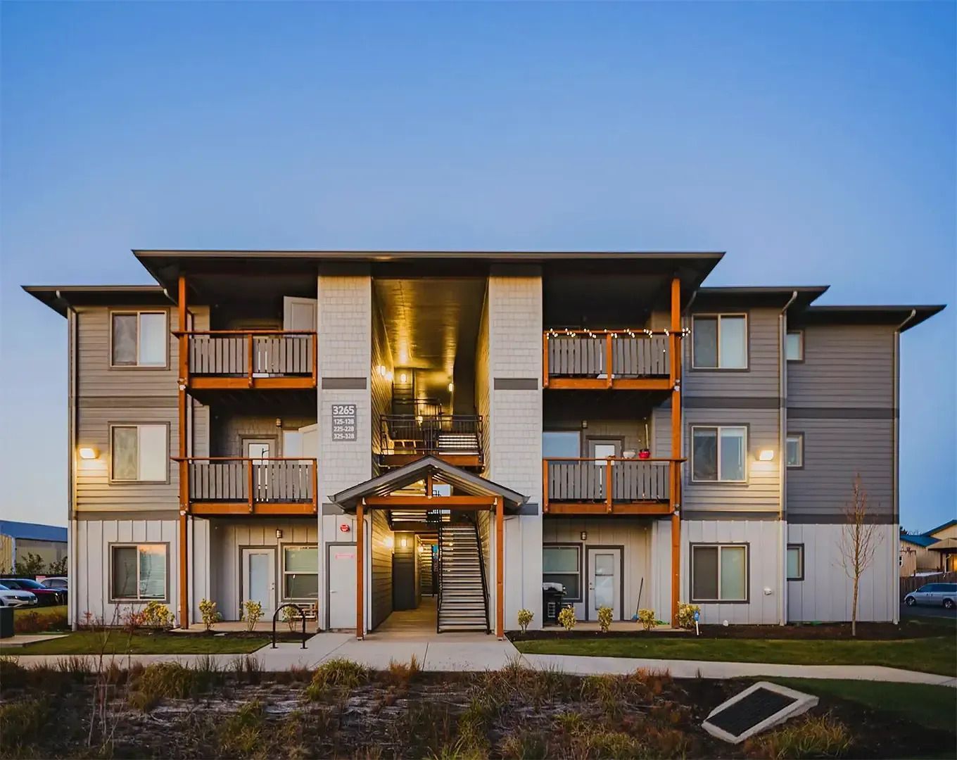Modern three-story apartment building with balconies and a central glass entrance at dusk