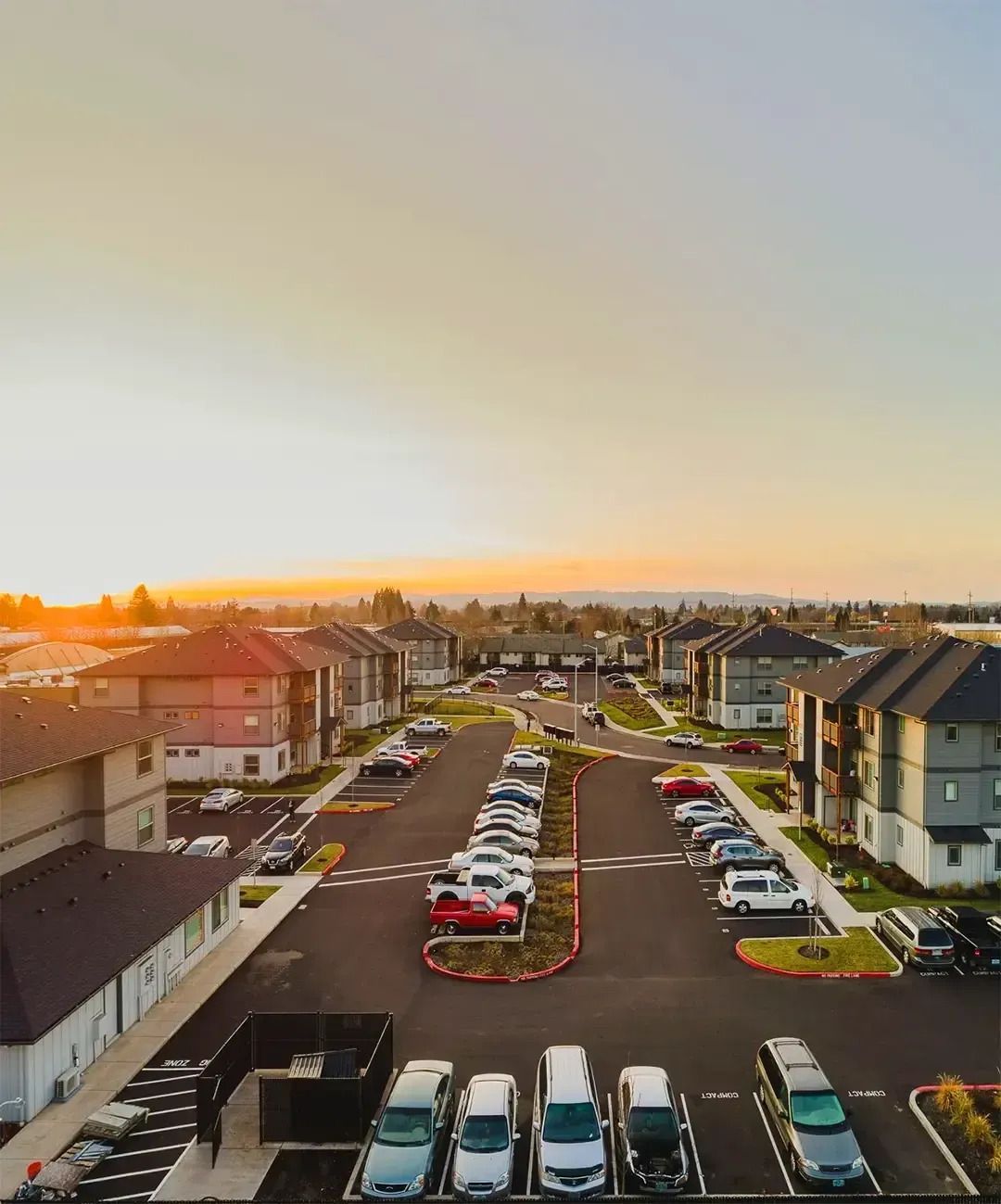 Apartment complex parking lot at sunset, with rows of cars and modern buildings under a clear sky