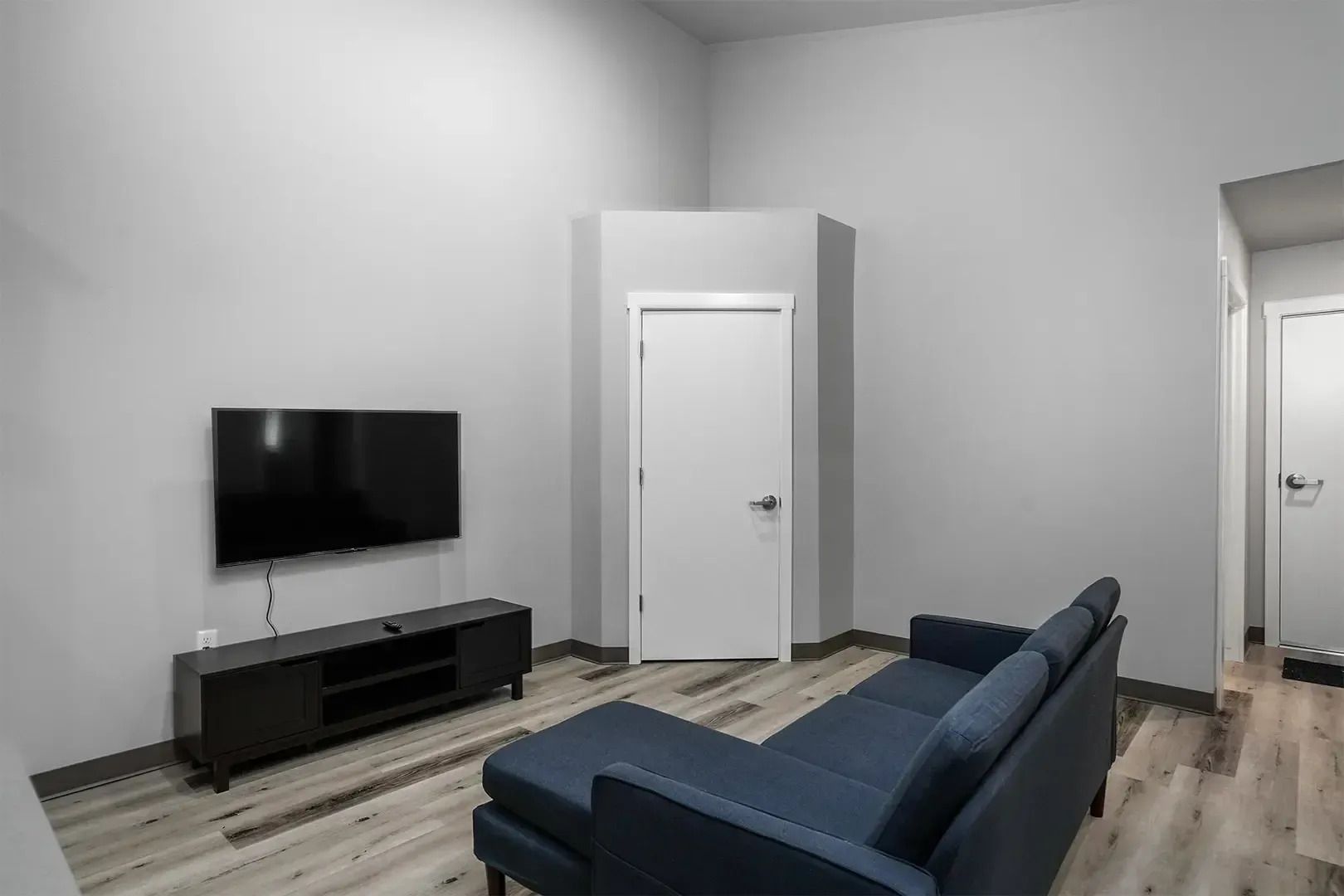 Modern living room with blue sofa, wall-mounted TV, white walls, and light wood flooring