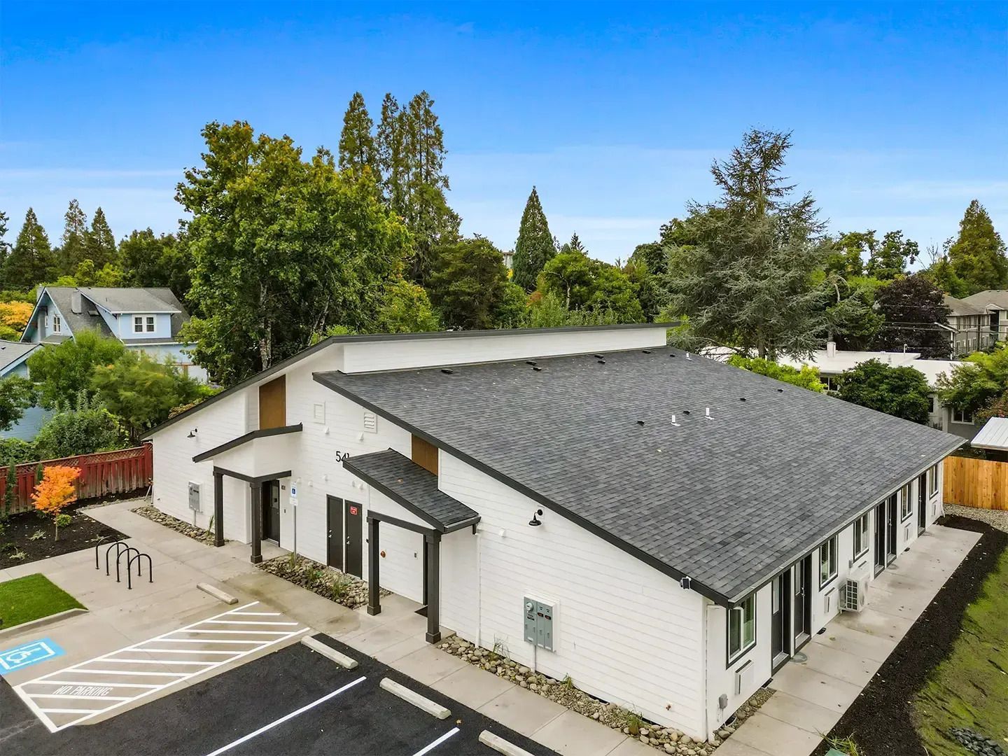 Aerial view of a white building with a gray roof, parking lot, and trees in a suburban area