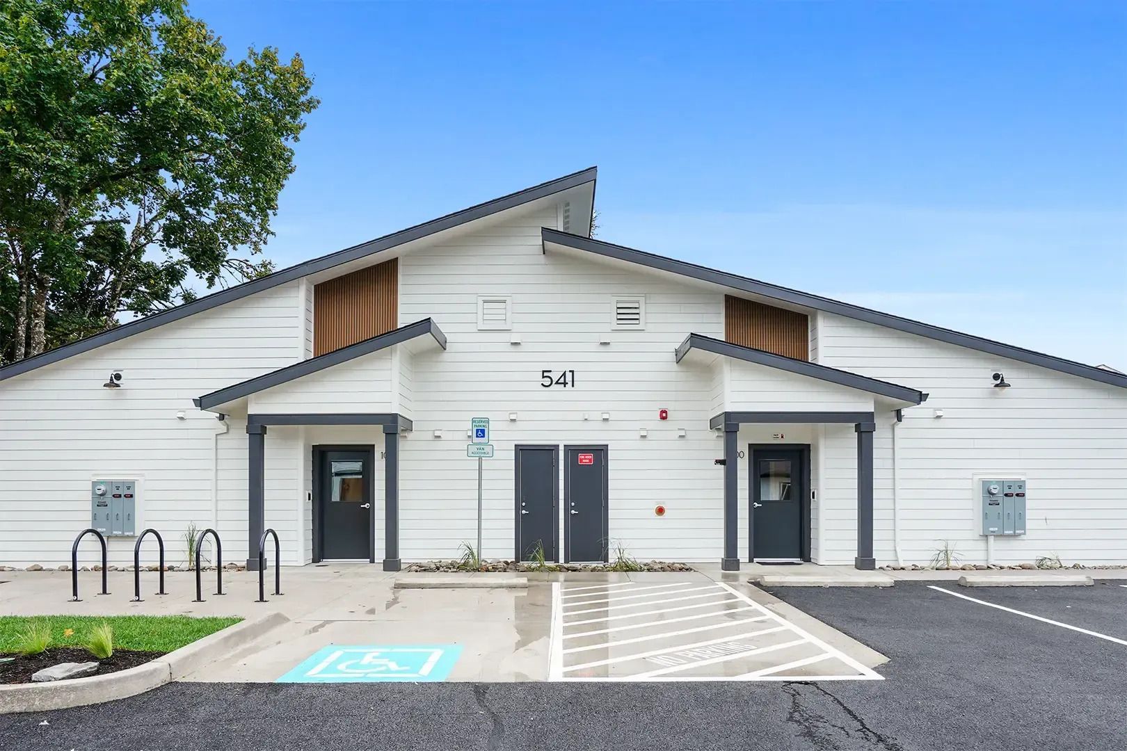 White building with two black doors, bike racks, and a paved entry under a blue sky