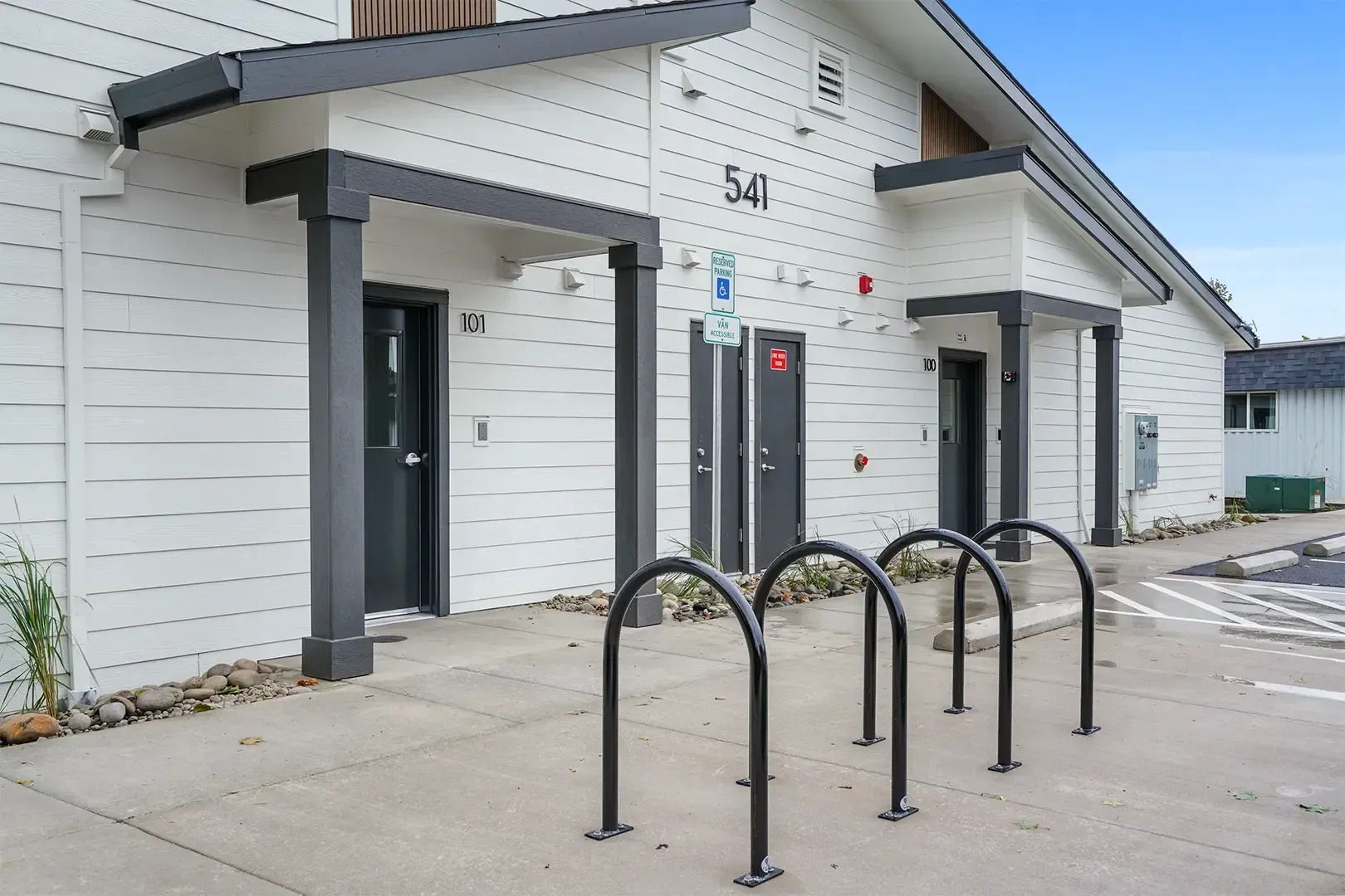 White apartment entrance with black bike racks and numbered doors on a sidewalk
