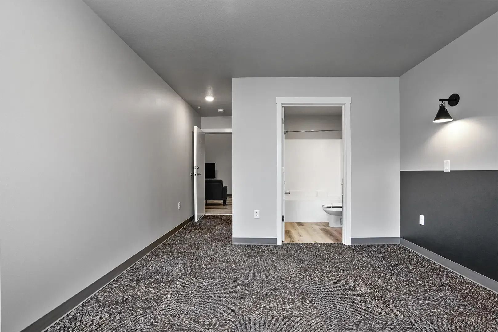 Empty carpeted room with gray walls, white closet, and hallway doorway under recessed lighting