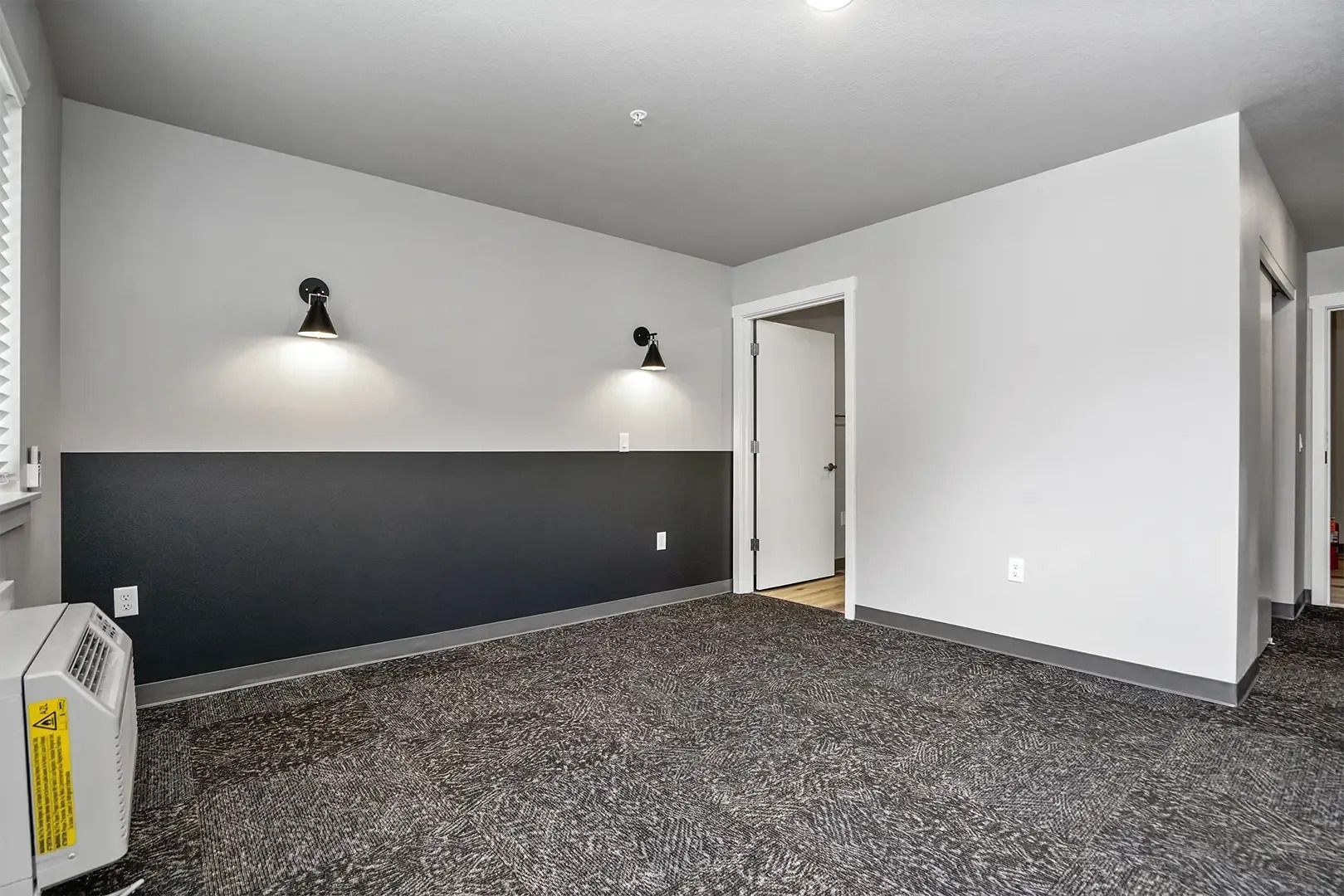 Empty carpeted bedroom with gray walls, dark accent wall, and open doorway to hall.