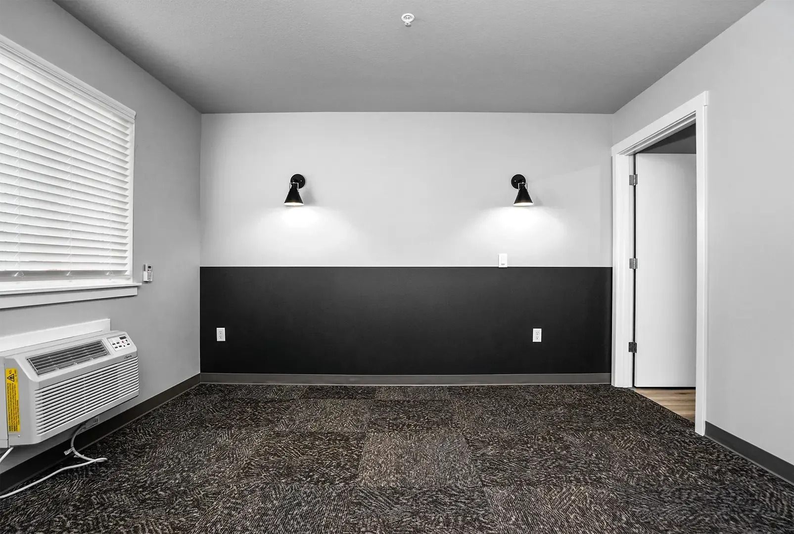 Empty gray room with dark accent wall, wall lights, window blinds, and open door