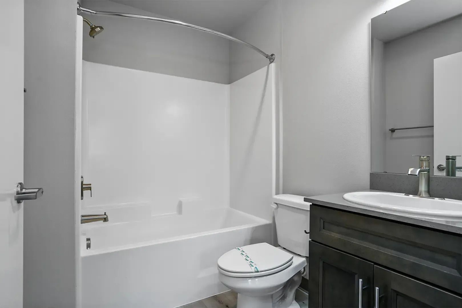 Small bathroom with white tub, toilet, sink, and dark vanity under a large mirror
