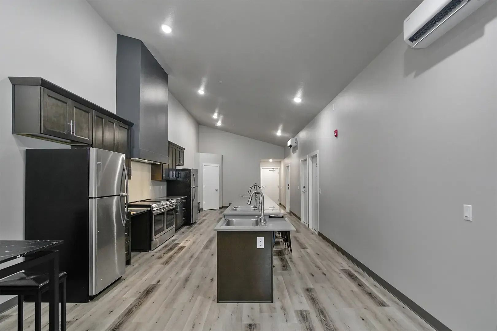 Modern kitchen with stainless steel appliances, gray cabinets, island, and light wood flooring
