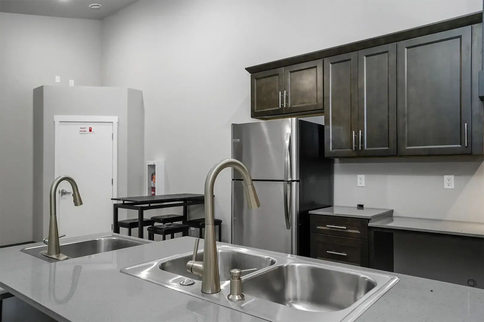 Modern kitchen with stainless steel appliances, dark cabinets, and a double sink on a gray island.