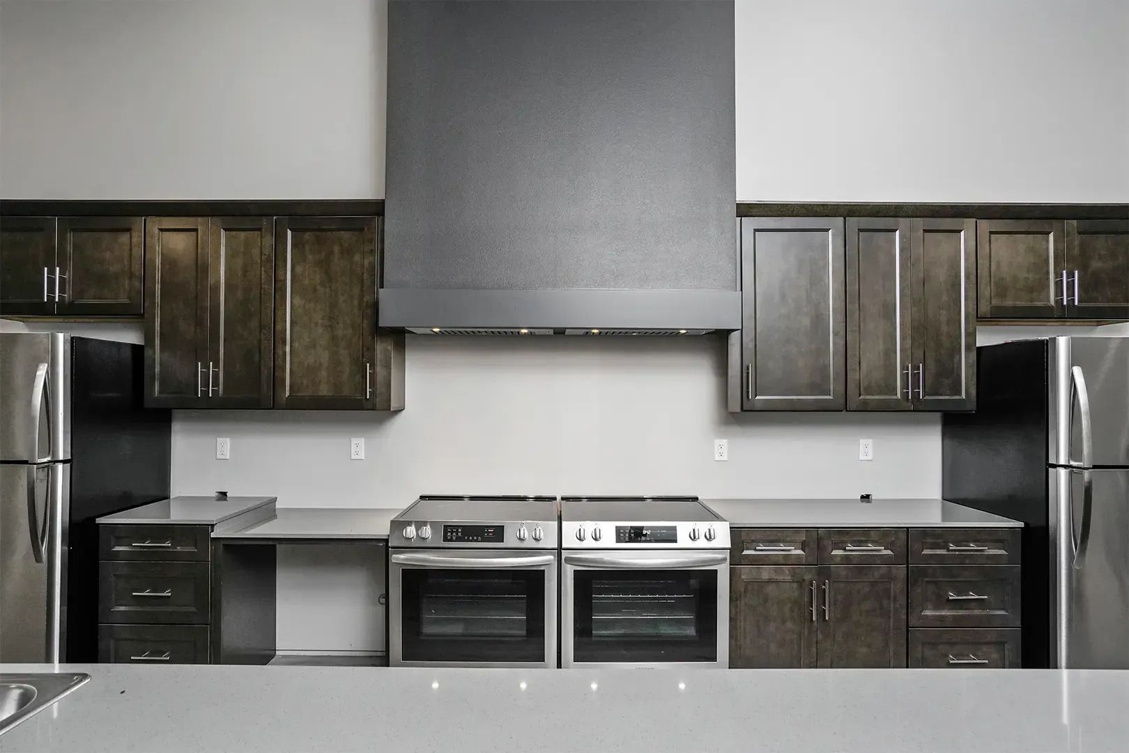 Modern kitchen with dark wood cabinets, stainless appliances, and a large gray range hood