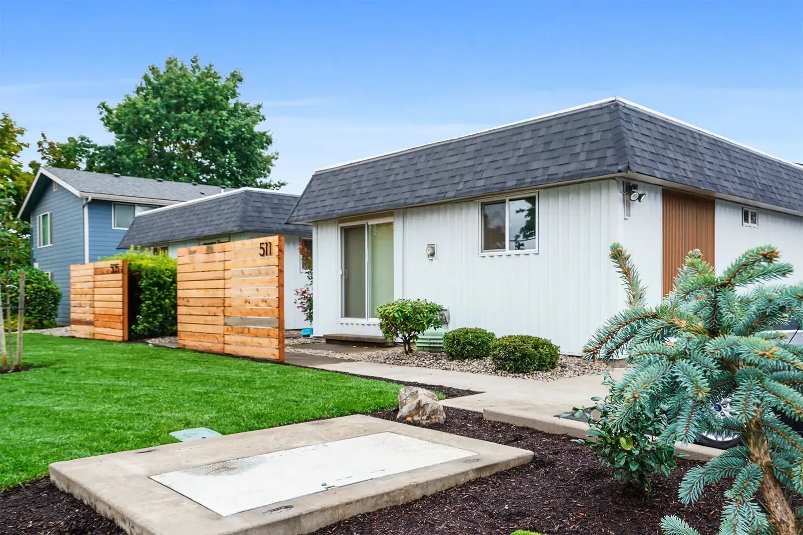 Modern single-story house with white exterior, wooden fence, and landscaped front yard