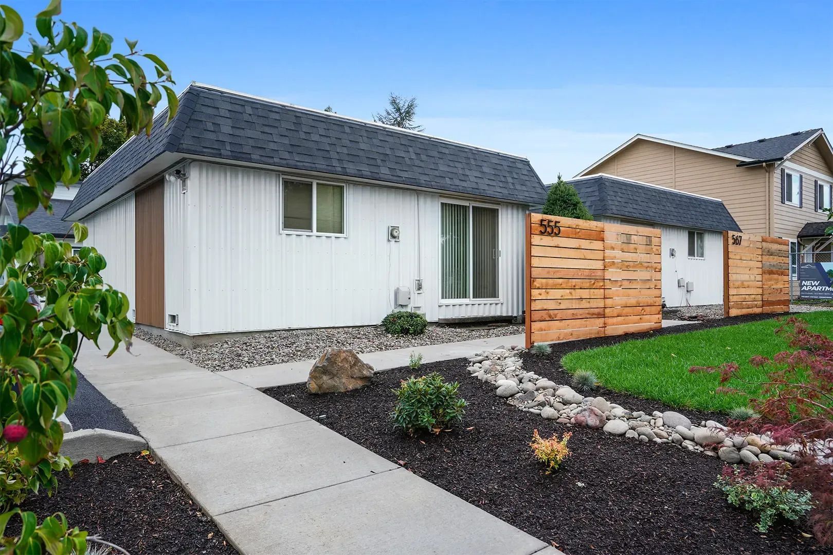 Modern white house with gray roof, front walkway, landscaped yard, and wooden fence gate