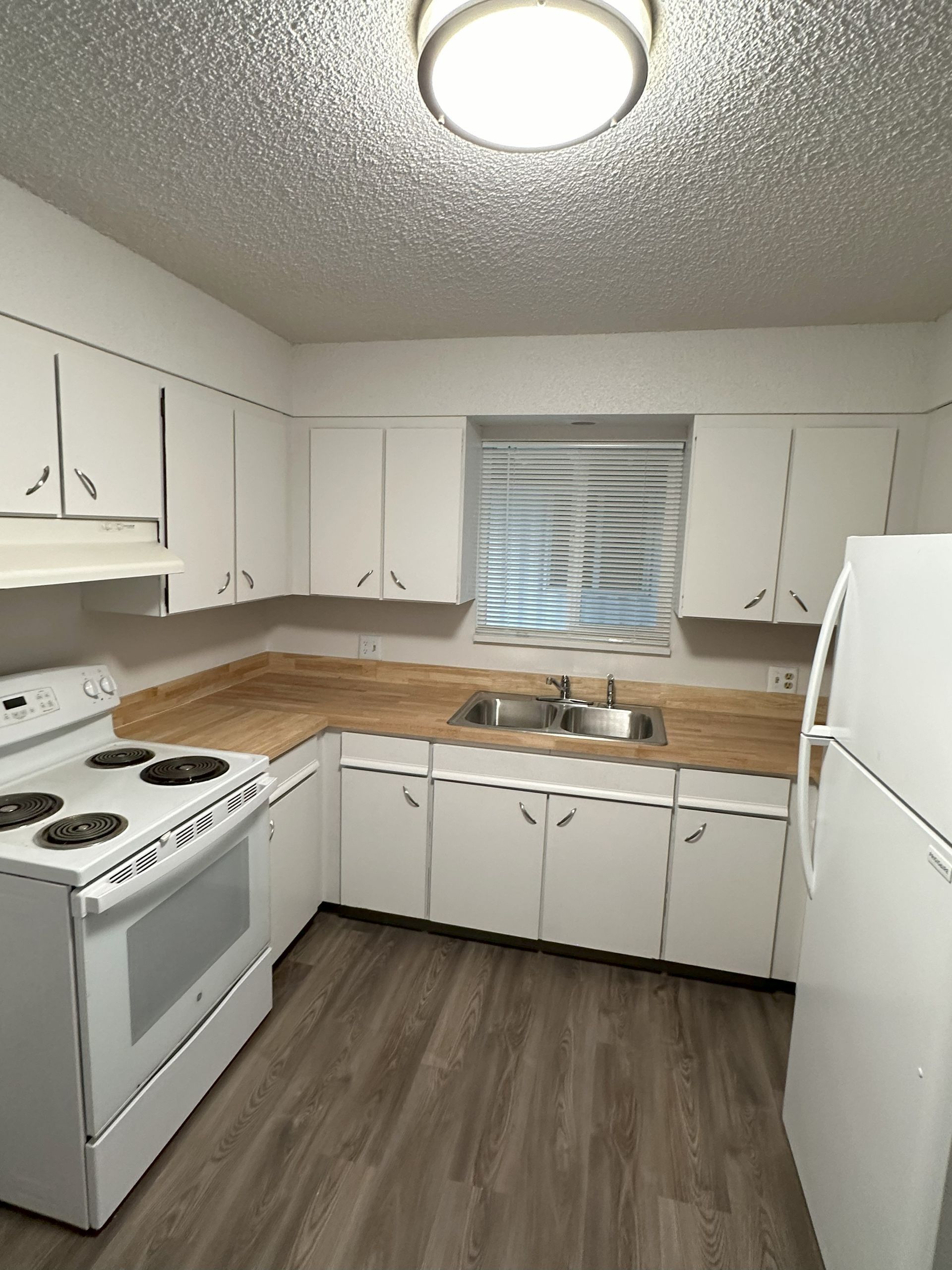 White kitchen with stove, sink, refrigerator, and wood countertops around a window with blinds
