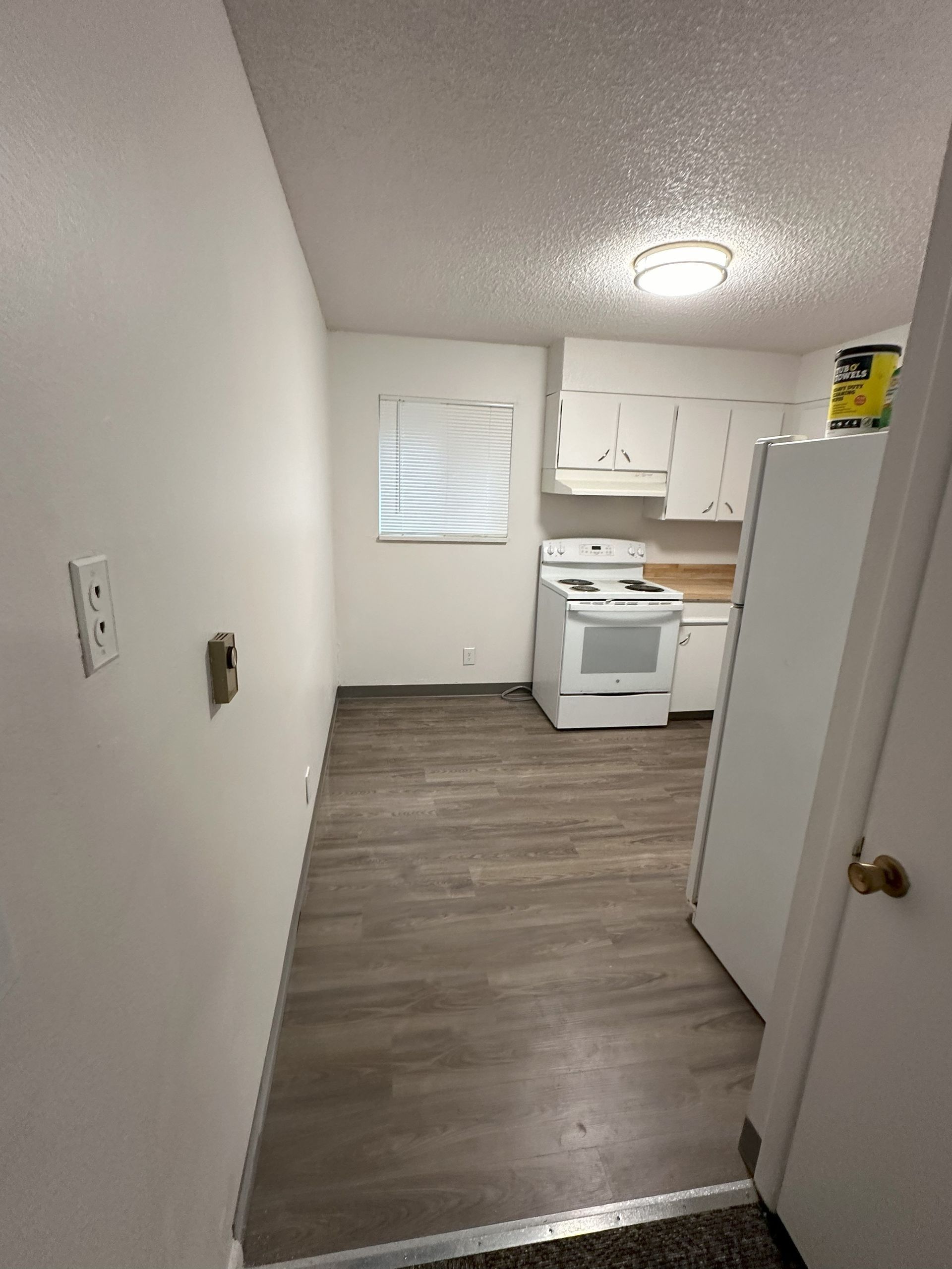 Empty apartment kitchen with white cabinets, stove, and wood-look flooring, viewed from a doorway