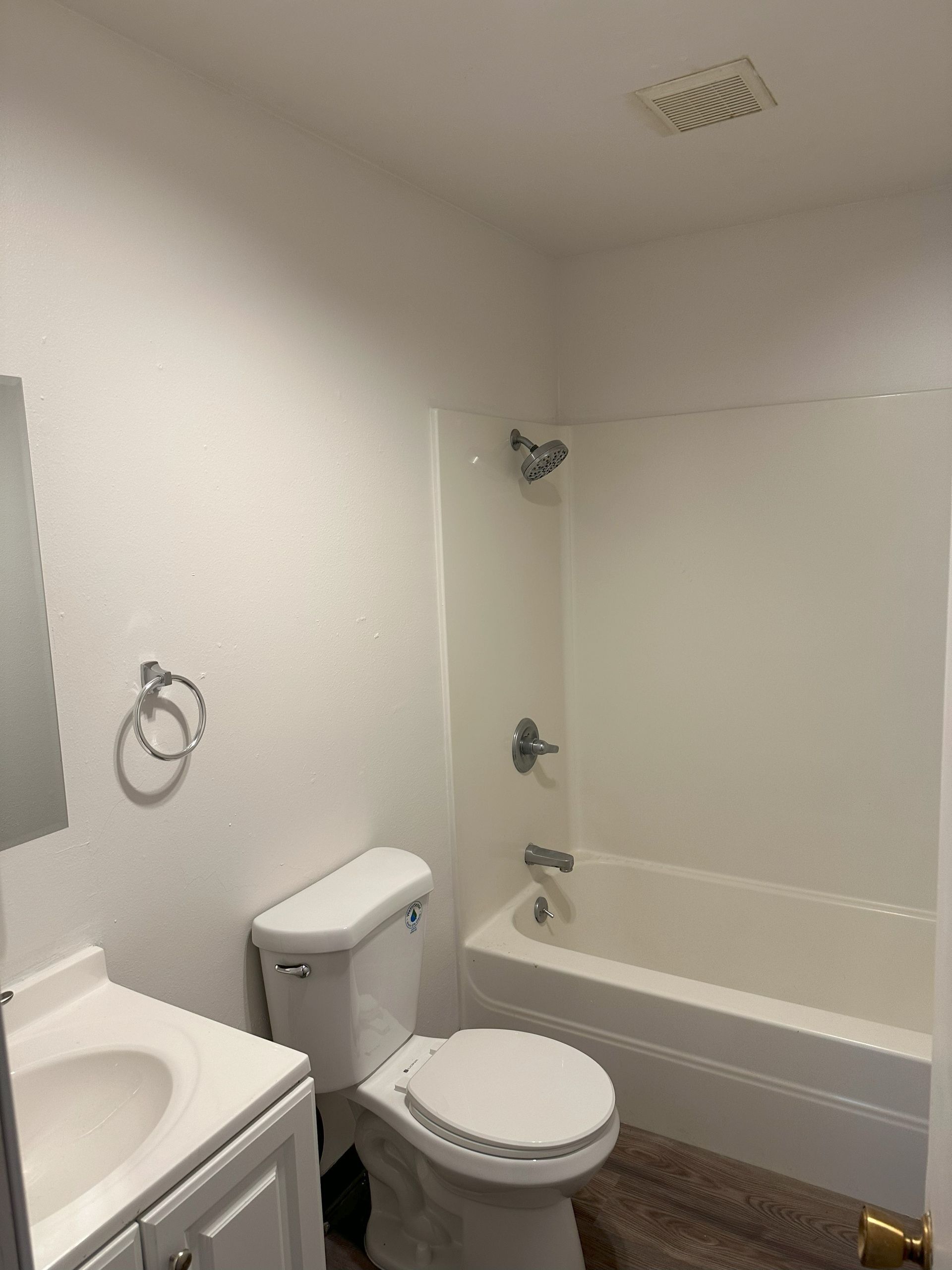Small white bathroom with toilet, sink, bathtub, mirror, and towel ring.