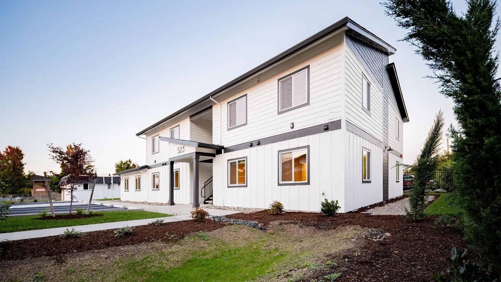 Modern white two-story house with dark roof and front yard at dusk