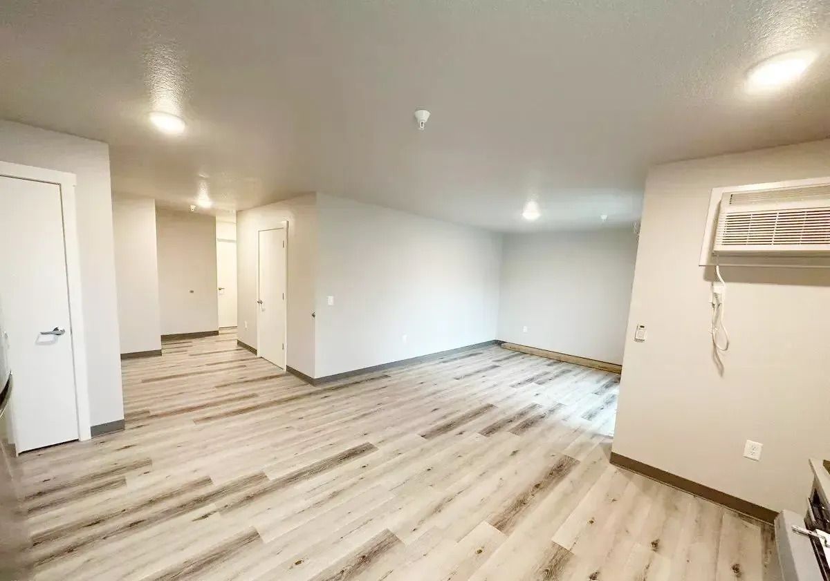 Empty modern room with light wood floors, white walls, recessed lights, and a wall-mounted intercom panel.