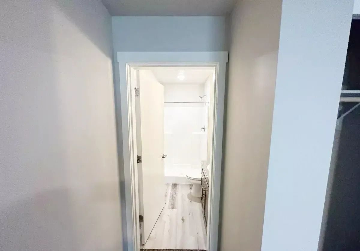 Narrow hallway with white walls leading to a bright room with an open door and tiled floor.