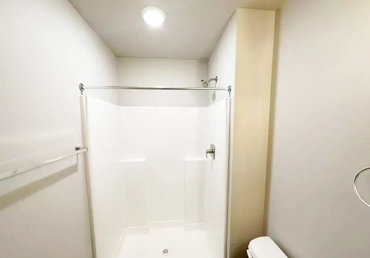 Small white bathroom with a shower stall, towel bar, and toilet visible.