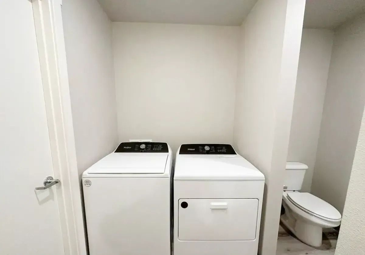 Laundry nook with a white washer and dryer beside a small toilet in a narrow alcove