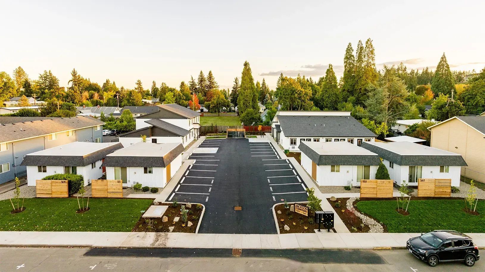 Aerial view of a suburban cul-de-sac with modern white houses, trees, and a parked black car.