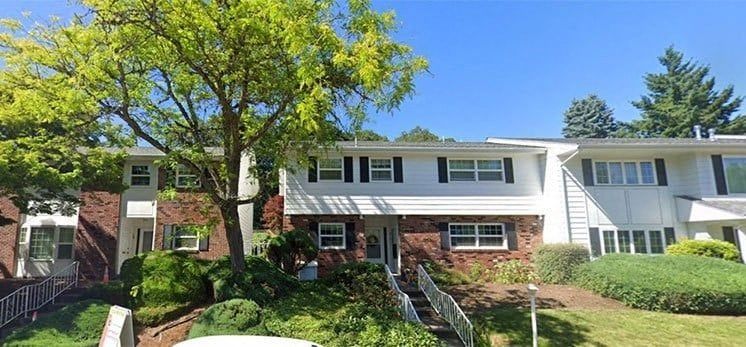 Brick townhouse with white siding, front lawn, trees, and a clear blue sky