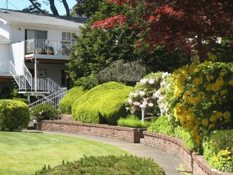 Suburban house with a curved brick garden wall, green lawn, and flowering shrubs in front yard