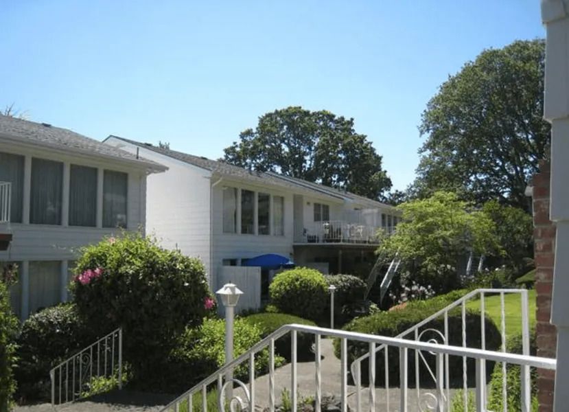 Apartment complex with white balconies, green shrubs, and a stair railing under a clear blue sky