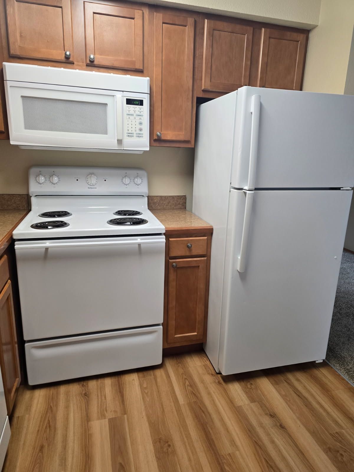 Small kitchen with white stove, microwave, and refrigerator, plus wood cabinets and flooring.